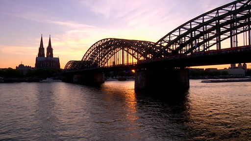 Die Hohenzollernbrücke in Köln mit Dom im Hintergrund bei Sonnenuntergang