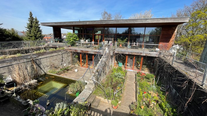 Blick auf ein großes Haus mit viel Glasflächen, davor ein Garten