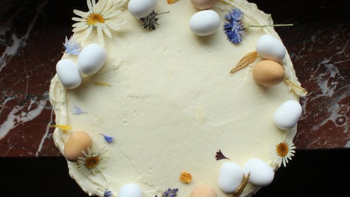 Ein Möhrenkuchen mit Frischkäseglasur, schön dekoriert mit Marzipaneiern und essbaren Blüten
