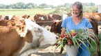 Anna Pröbstle mit Kühen und einem Eimer voller Wildblumen. 
