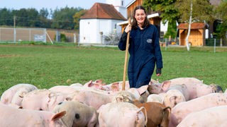 Katharina Mühlbauer auf der Weide umringt von Schweinen. 
