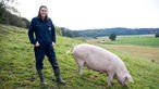Katharina Mühlbauer auf der Weide, neben ihr ein Schwein. 
