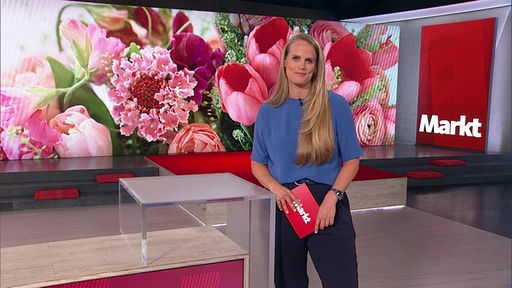 Das Bild zeigt Svenja Kellershohn im Markt-Fernsehstudio. Im Hintergrund sind bunte Blumen abgebildet. 