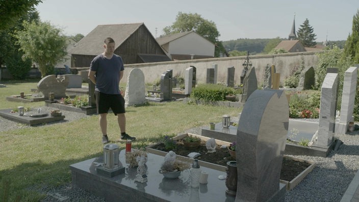 Jonas steht auf Friedhof vor dem Grab seiner Mutter