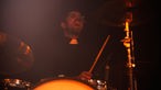 Schlagzeuger von Angelika Express im Dunkeln hinter seinem Schlagzeug singt inbrünstig ins Mikrofon