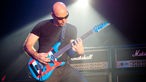 Joe Satriani beugt sich beim Spielen über seine Gitarre