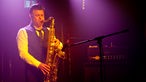 Saxophonist spielt im lila-gelben Licht der Scheinwerfer.