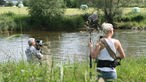 Das Rockpalastteam an der Weser, wie sie Filmaufnahmen machen, vorne die Tonfrau, hinten am Fluss der Kameramann