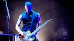 Gitarrist wird von blauem Licht beleuchtet und spielt eine holz-farbene E-Gitarre