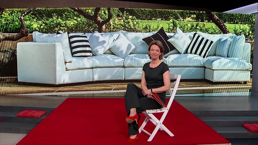 Das Bild zeigt Anna Planken sitzen im Markt-Fernsehstudio. Im Hintergrund sind Gartenmöbel abgelichtet.