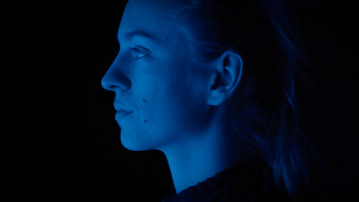 Profilportrait einer Frau, deren Gesicht blau angeleuchtet ist, der Hintergrund ist schwarz