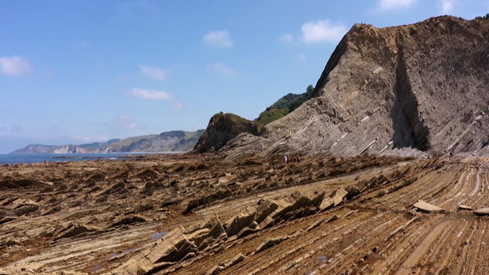 Ebene mit aufgeschichteten Gesteinen, im Hintergrund steil abfallende Küste