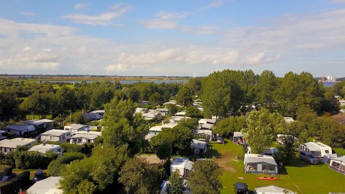 Blick über Campingplatz mit Hauszelten und Wohnwagen zwischen Bäumen 