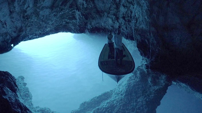 Kleines Boot mit zwei Personen in einer Grotte mit blauem Wasser