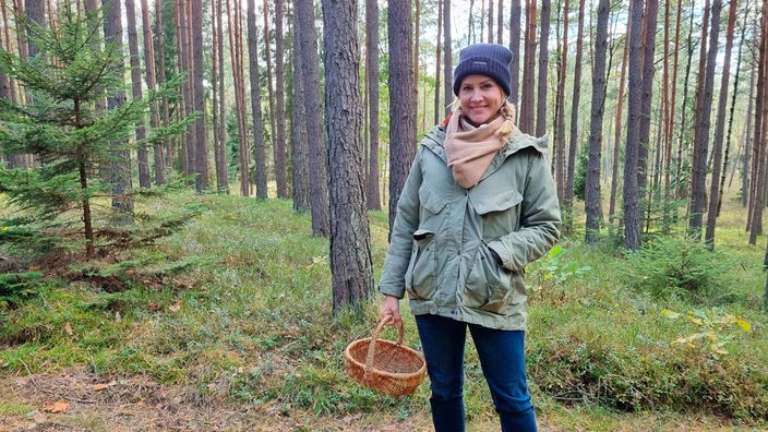 Judith Rakers steht mit einem Körbchen in der Hand im Wald