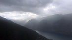 Blick von Berggipfel auf wolkenverhangenen Fjord