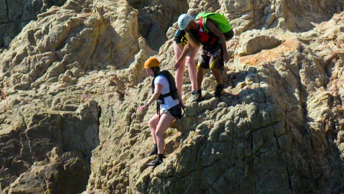 Drei Personen klettern an einem Felshang