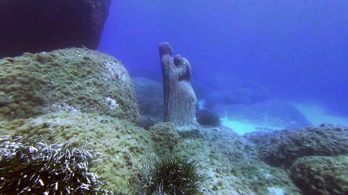 Eine Madonnen-Statue steht auf felsigem Meeresgrund