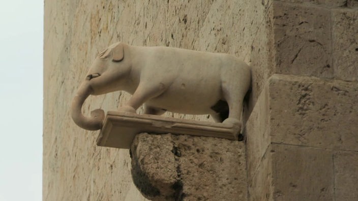 Eine Elefantenstatue steht auf  einer Brüstung an einer Mauer
