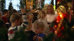 Das Christkind empfängt viele Kinder in einem geschmückten Raum