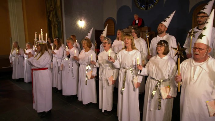 Chormitglieder in weißen Gewändern und mit Kerzen singen in einer Kirche