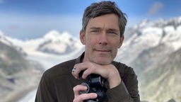 Christian Klepp mit Kamera vor einem Gebirgspanorama