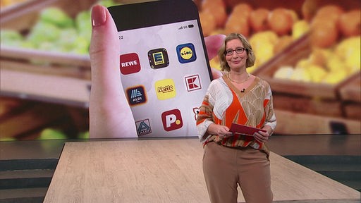 Die Moderatorin Yvonne Willicks steht im Servicezeit-Fernsehstudio. Im Hintergrund sieht man ein Bild von einer Person, die ein Smartphone in der Hand hat.